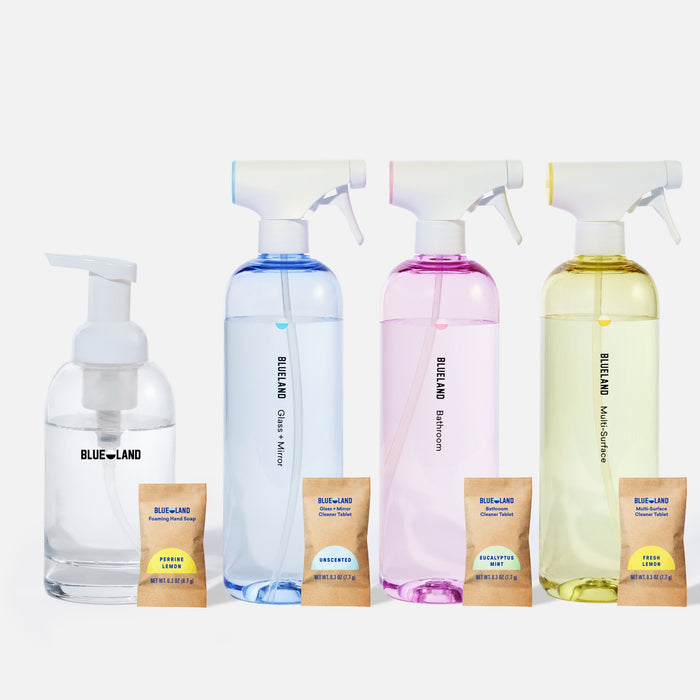 Four clear bottles of BlueLand cleaning products, each with a labeled spray or foaming pump, are displayed in a row with four corresponding refill packets in front of them on a white background.